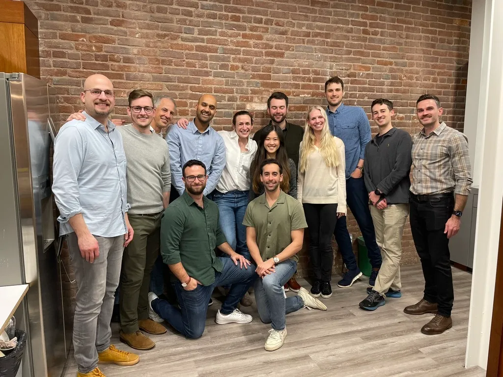 Group of adults posing together indoors against a brick wall